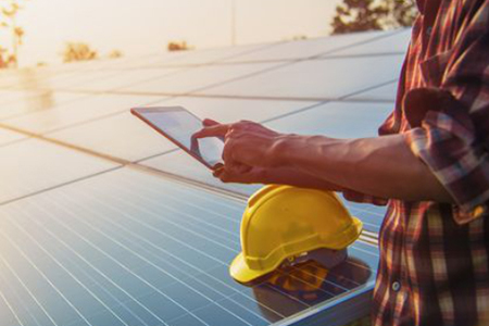 Vor einer PV-Anlage prüft eine Person etwas auf einem Tablet.